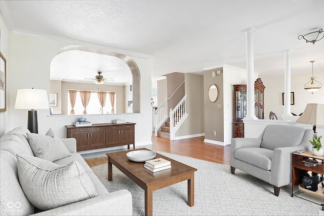 living area featuring a ceiling fan, stairway, decorative columns, and light wood-style floors