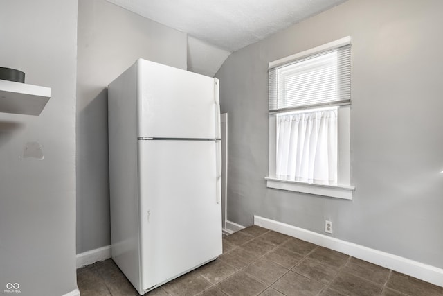 kitchen featuring tile patterned floors, baseboards, freestanding refrigerator, and vaulted ceiling