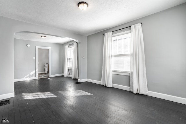 unfurnished room featuring visible vents, baseboards, dark wood finished floors, arched walkways, and a textured ceiling