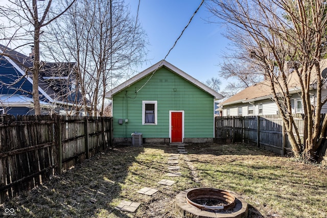 rear view of house with cooling unit, a fire pit, a fenced backyard, and a yard