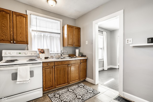 kitchen featuring tile patterned floors, white electric range, brown cabinets, and a sink