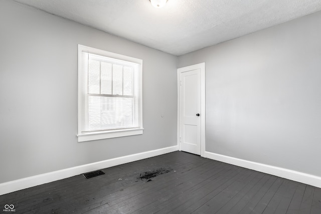 spare room featuring dark wood finished floors, visible vents, a textured ceiling, and baseboards