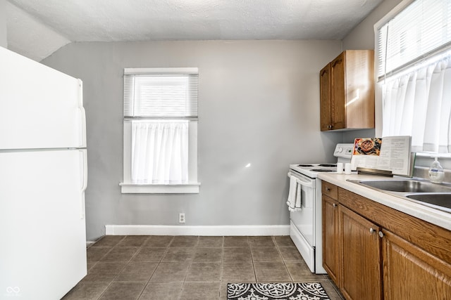 kitchen featuring brown cabinets, a textured ceiling, white appliances, light countertops, and baseboards