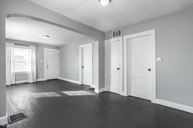 interior space with visible vents, baseboards, arched walkways, dark wood-type flooring, and a textured ceiling