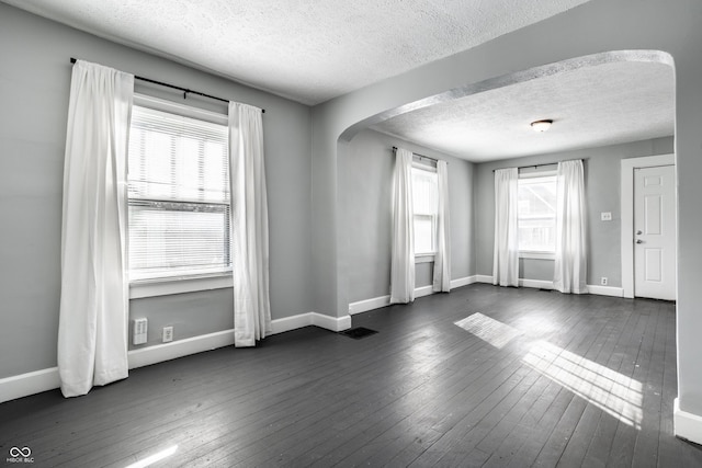 unfurnished room with a healthy amount of sunlight, arched walkways, and dark wood-style flooring