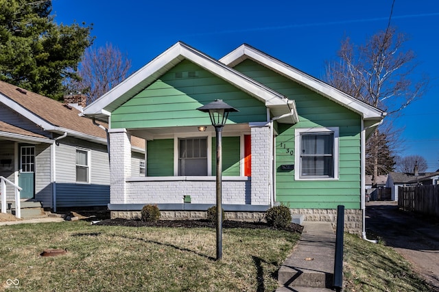 bungalow-style house featuring a front yard, fence, brick siding, and covered porch