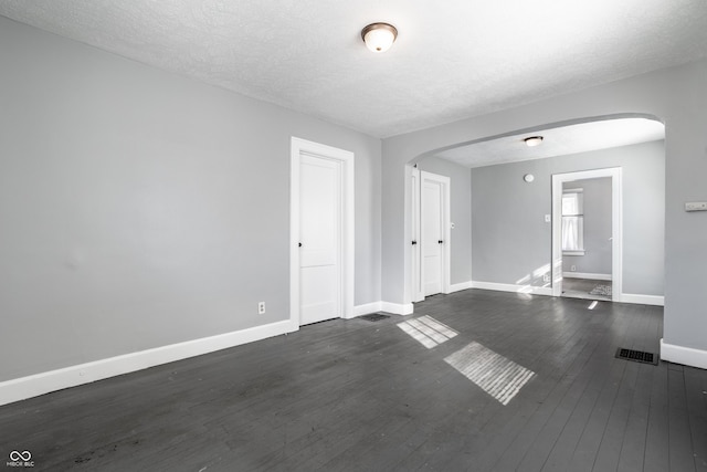 unfurnished room featuring arched walkways, visible vents, dark wood-type flooring, and baseboards