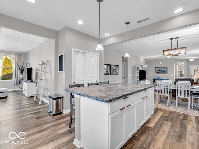 kitchen with pendant lighting, a kitchen island, visible vents, and white cabinets