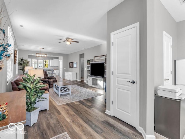 living room featuring ceiling fan with notable chandelier, visible vents, baseboards, and wood finished floors