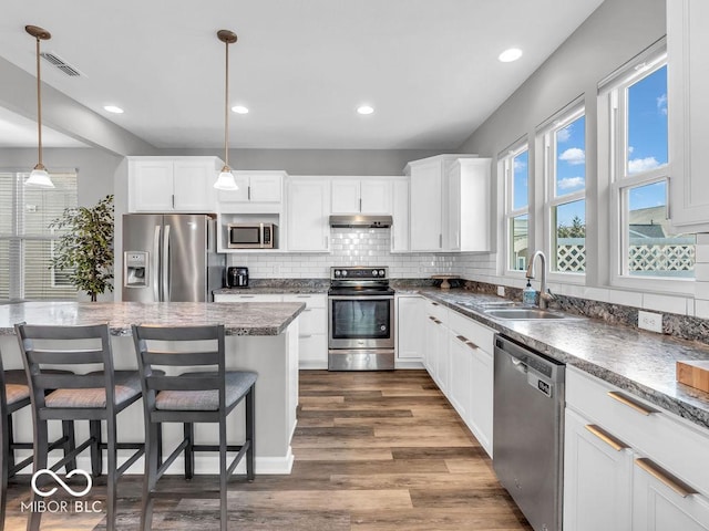 kitchen featuring appliances with stainless steel finishes, white cabinets, hanging light fixtures, and under cabinet range hood