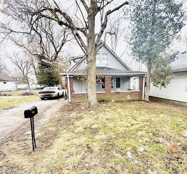 bungalow with driveway, covered porch, a front lawn, and brick siding