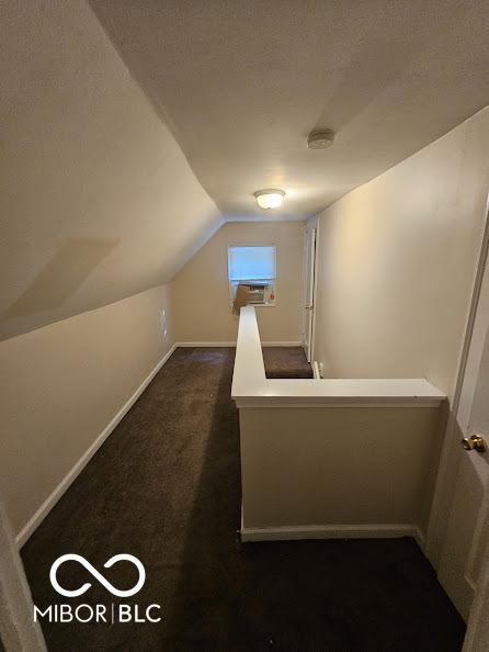 additional living space featuring dark carpet, vaulted ceiling, and baseboards