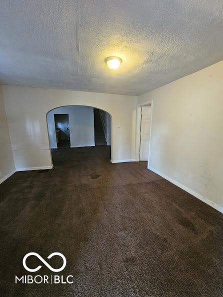 spare room featuring arched walkways, carpet floors, a textured ceiling, and baseboards