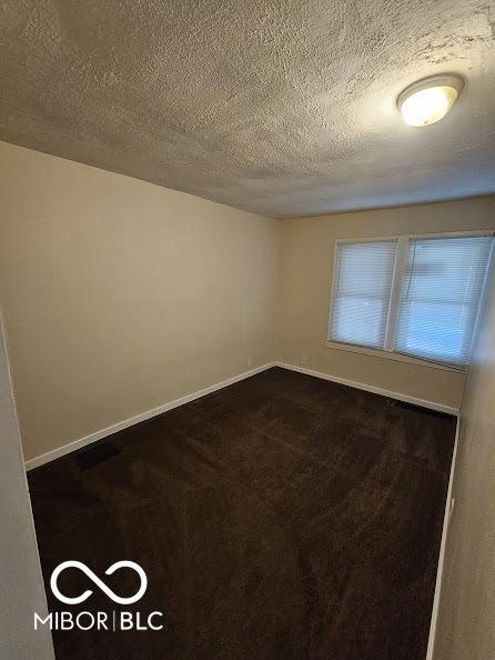 unfurnished room featuring dark carpet, baseboards, and a textured ceiling