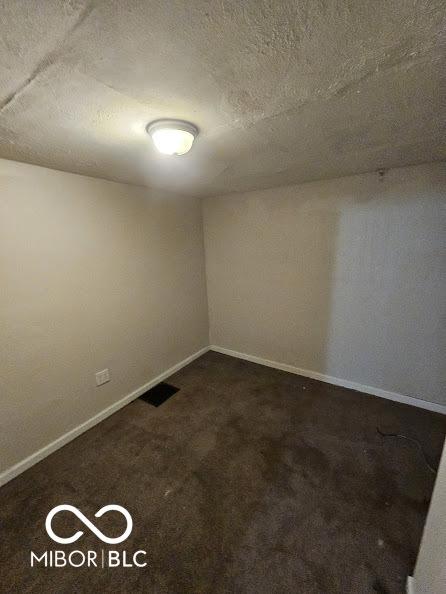 empty room with baseboards, dark colored carpet, and a textured ceiling