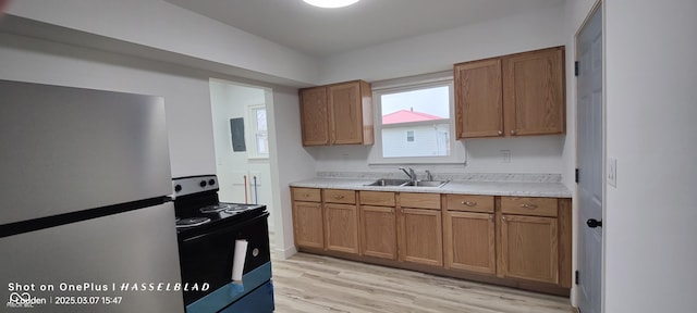 kitchen featuring a sink, brown cabinets, black range with electric stovetop, and freestanding refrigerator