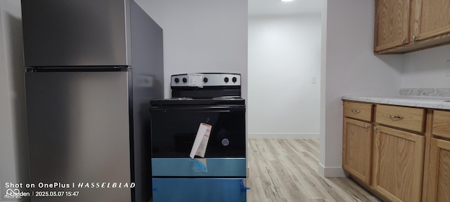 kitchen featuring light wood-type flooring, black range with electric stovetop, freestanding refrigerator, light countertops, and baseboards