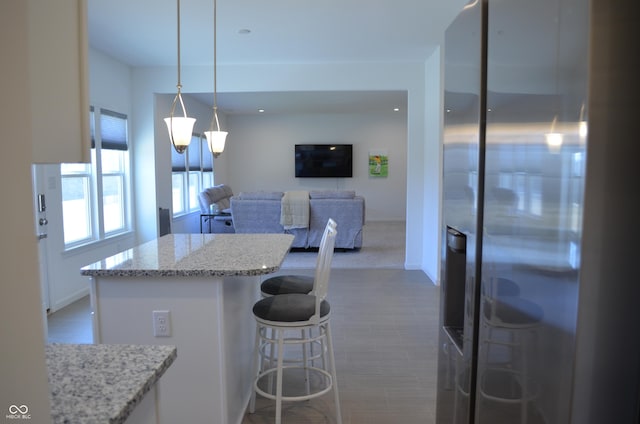 kitchen with a kitchen breakfast bar, hanging light fixtures, stainless steel refrigerator with ice dispenser, and light stone countertops