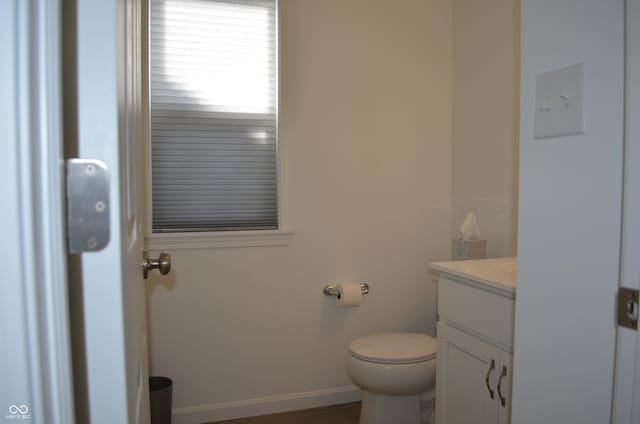 half bath featuring vanity, toilet, and baseboards