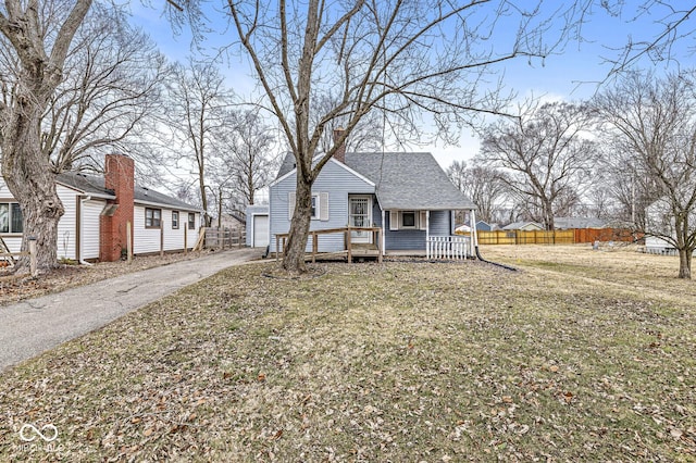 bungalow-style house with a shingled roof, an outdoor structure, fence, a chimney, and a front yard