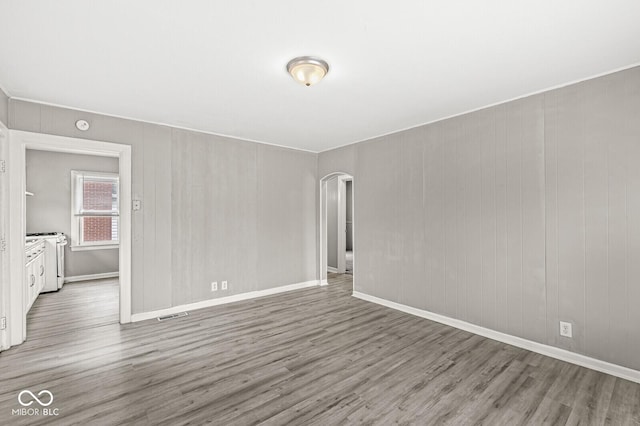 spare room with baseboards, visible vents, arched walkways, and wood finished floors