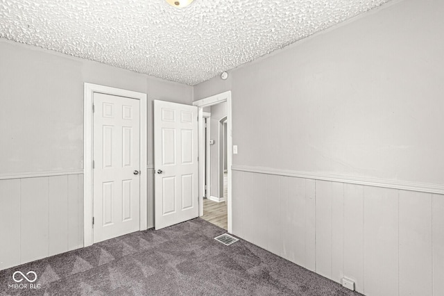 unfurnished bedroom with a textured ceiling, a wainscoted wall, carpet flooring, visible vents, and a closet