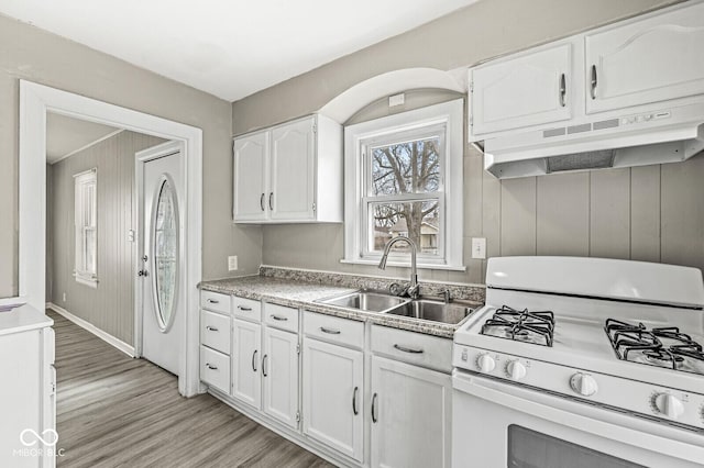 kitchen with white gas range oven, light wood-style floors, under cabinet range hood, white cabinetry, and a sink