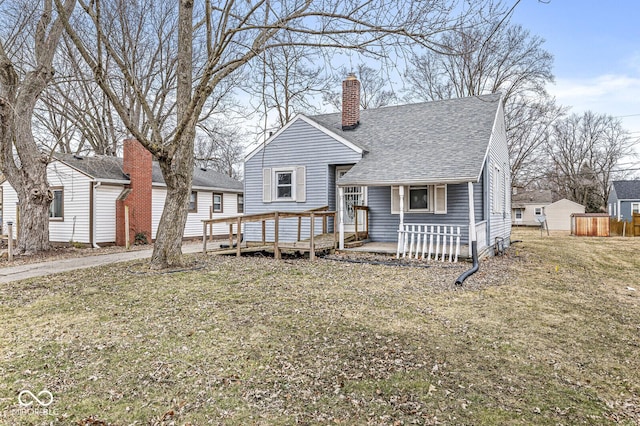 view of front of property featuring a deck, roof with shingles, a chimney, and a front lawn