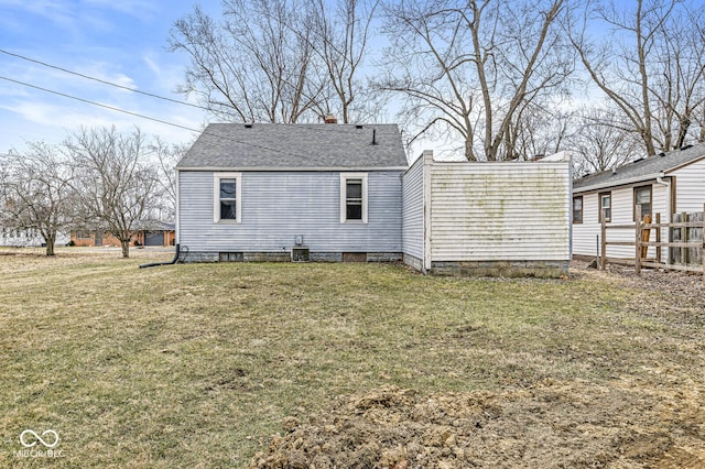 back of house featuring a shingled roof, fence, and a lawn