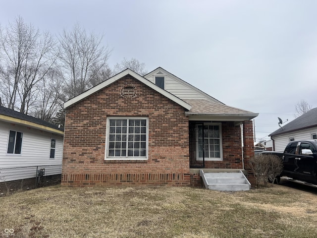 exterior space featuring a shingled roof, fence, a lawn, and brick siding