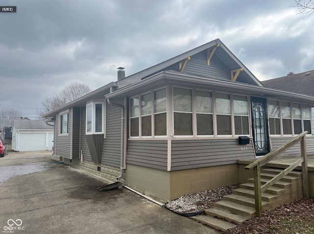 view of front facade with concrete driveway, a chimney, an outdoor structure, and a sunroom