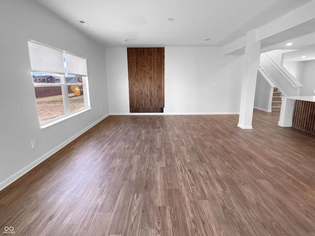 unfurnished living room with stairs, baseboards, and wood finished floors