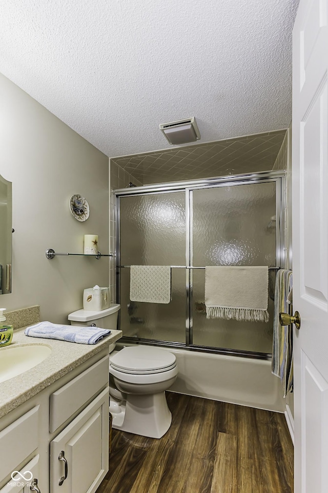 bathroom with toilet, shower / bath combination with glass door, wood finished floors, a textured ceiling, and vanity