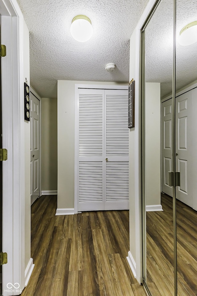 hall with a textured ceiling, dark wood-style flooring, and baseboards