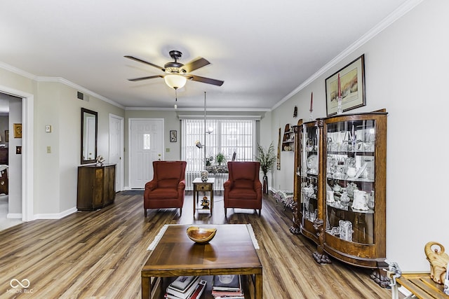 living area with ornamental molding, wood finished floors, and a ceiling fan