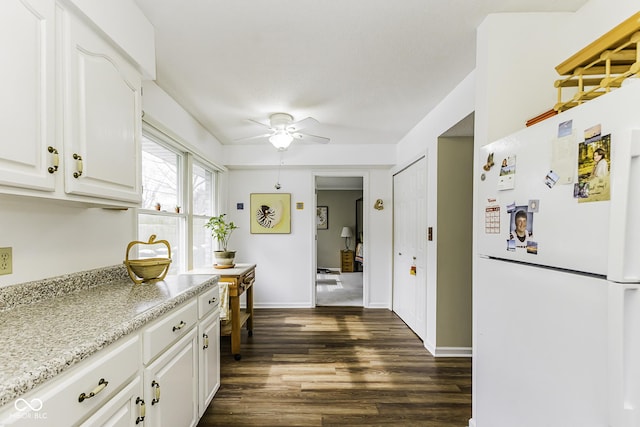 kitchen with dark wood-type flooring, freestanding refrigerator, a ceiling fan, white cabinetry, and baseboards