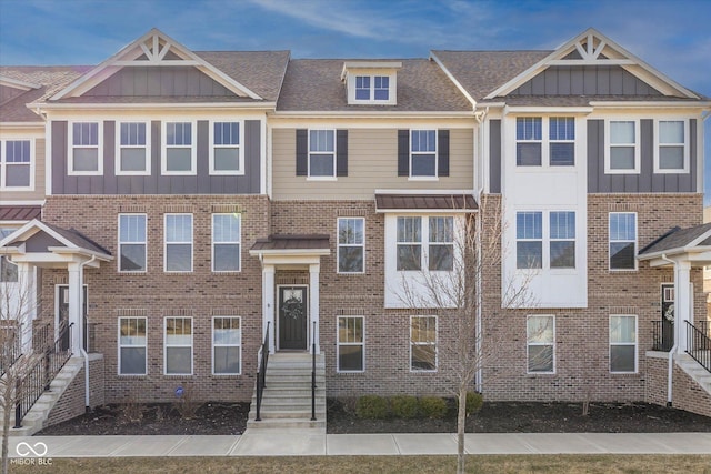 townhome / multi-family property featuring board and batten siding, brick siding, and a shingled roof