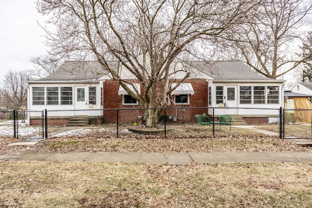 view of front of home featuring a shingled roof, a sunroom, a fenced front yard, a gate, and brick siding