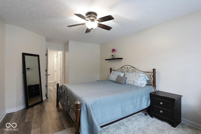 bedroom featuring a ceiling fan, a textured ceiling, baseboards, and wood finished floors