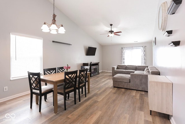 dining room featuring light wood-style floors, baseboards, high vaulted ceiling, and ceiling fan with notable chandelier