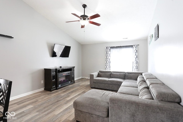 living area with light wood finished floors, baseboards, a glass covered fireplace, ceiling fan, and vaulted ceiling