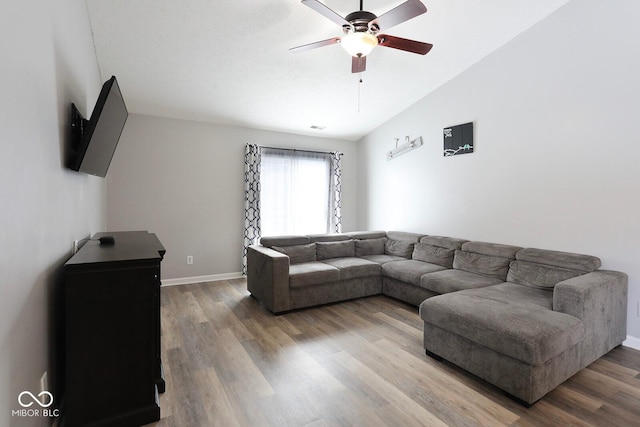 living area with a ceiling fan, vaulted ceiling, light wood-style flooring, and baseboards