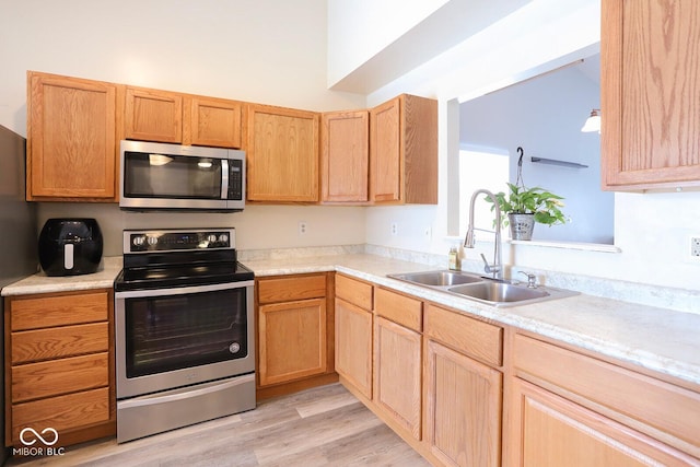 kitchen featuring light countertops, appliances with stainless steel finishes, a sink, and light wood-style floors