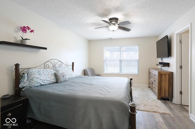 bedroom with light wood-type flooring, ceiling fan, baseboards, and a textured ceiling