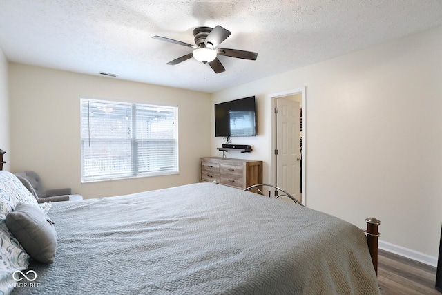 bedroom featuring a ceiling fan, visible vents, a textured ceiling, and wood finished floors