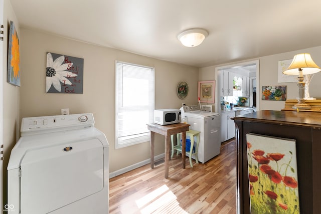 laundry area with laundry area, separate washer and dryer, a wealth of natural light, and light wood-style floors