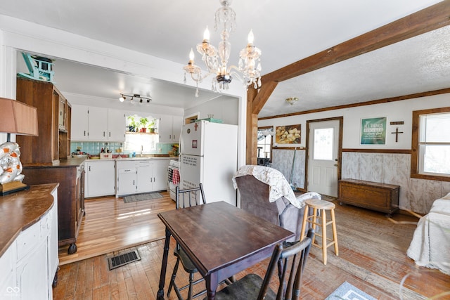 dining space featuring visible vents, wainscoting, ornamental molding, beamed ceiling, and light wood-type flooring