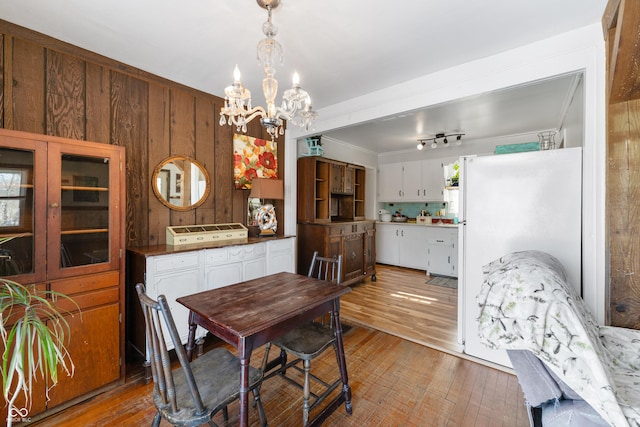 dining space featuring light wood-style flooring, wooden walls, crown molding, and a notable chandelier