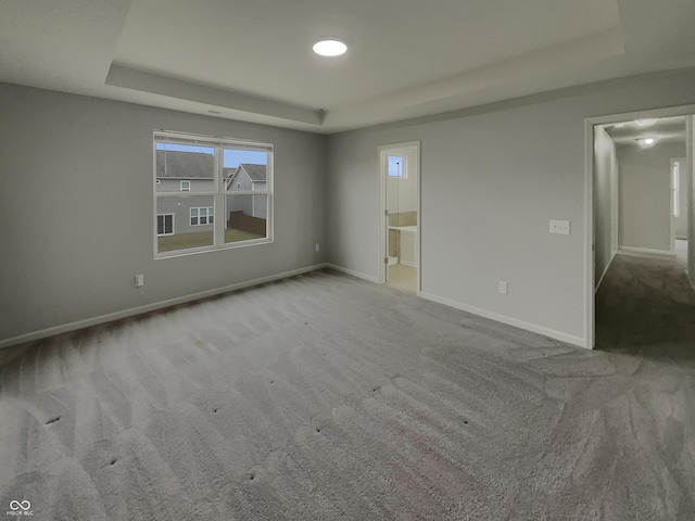 carpeted spare room with recessed lighting, a raised ceiling, and baseboards