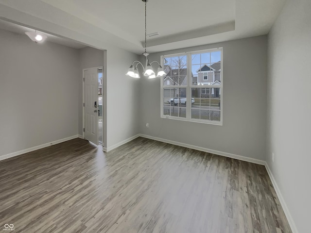 unfurnished dining area with visible vents, baseboards, wood finished floors, a tray ceiling, and a notable chandelier